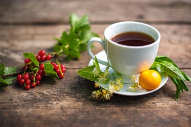 Beyaz bardakta çay, ahşap bir masada, bir çileğin etrafında, çilek, nane