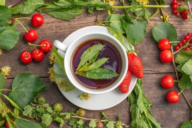 Beyaz bardakta çay, ahşap bir masada, bir çileğin etrafında, çilek, nane