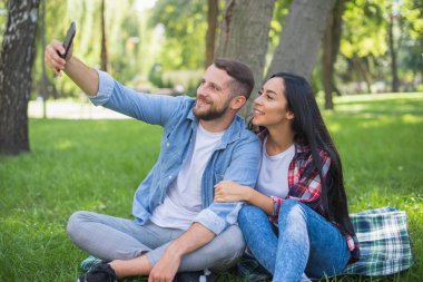 parkta bir ekose battaniye üzerinde oturan sevgi dolu çift ve telefon, yakışıklı adam ve kız kullanın