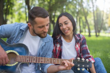 adam ve kız parkta gitar çalmak, ağacın yanında çim oturup
