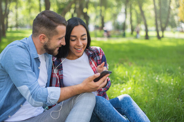 loving couple sitting on a plaid blanket in the park and use the phone, handsome guy and girl