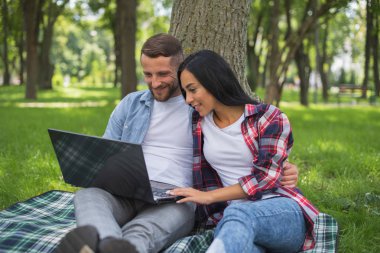 parkta sevgi dolu çift bir dizüstü bilgisayar kullanıyor, sarılma