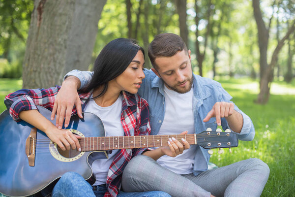 guy and girl play the guitar in the park, sit on the grass near the tree