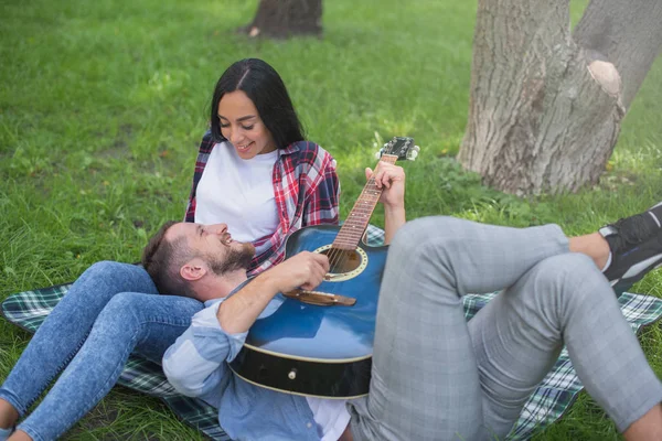 guy and girl play the guitar in the park, sit on the grass near the tree