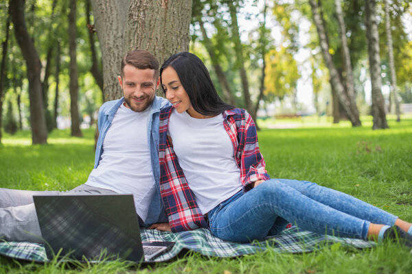 любящая пара в парке пользуется ноутбуком, обнимается
