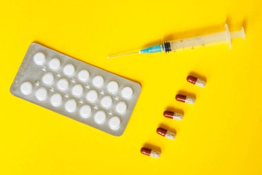 Sağlık sorunları. Beyaz Tablet, kapsül ve bir şırınga yalan üzerine sarı bir arka plan ile blister.