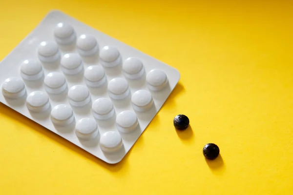 White packing of tablets - a blister and two black tablets lie on a yellow background