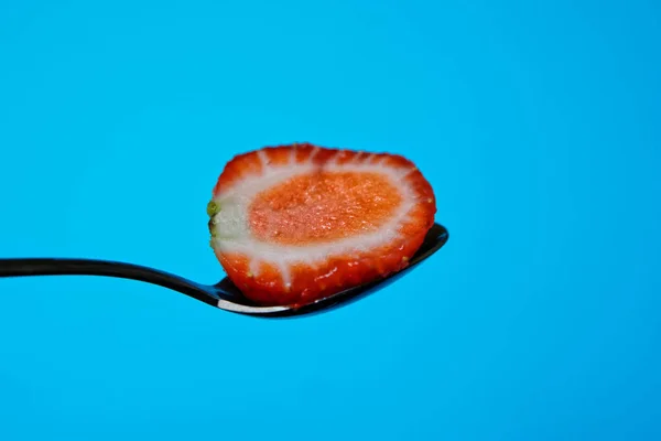 Metade de um morango está em uma colher em um fundo azul . — Fotografia de Stock