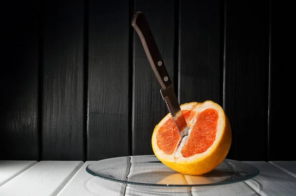 Pamplemousse et couteau dans une assiette transparente avec un fond en bois naturel . — Photo