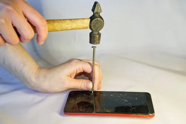 A man hammers a nail into the screen of a smartphone. Features of breakage, warranty and repair
