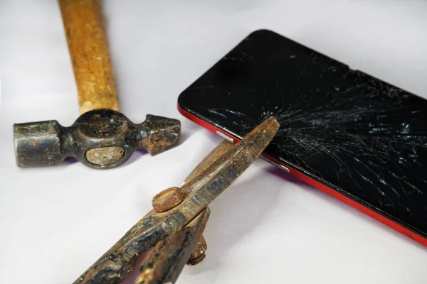 Smartphone con pantalla rota, tijeras de metal y martillo sobre fondo blanco . — Foto de Stock