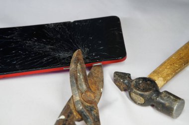 Smartphone with a broken display, metal scissors and a hammer on a white. Features of breakage and repair                            clipart