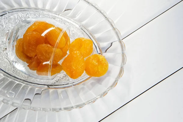 Fruits secs - abricots dans une assiette transparente sur une surface en bois blanc. Vue d'en haut. Gros plan . — Photo