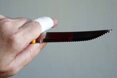 Yaralı parmak ile bir adamın elinde keskin bir bıçak. Hafif bir arka plan üzerinde. Tehlike ve tehdit.                    