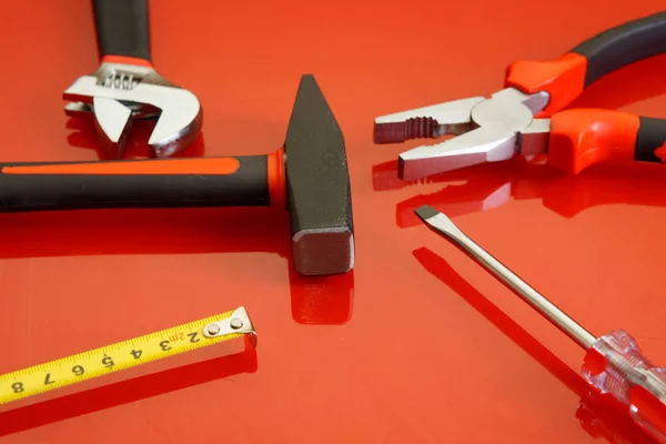 Pliers, tape measure, screwdriver, hammer and adjustable wrench lie on a red polished surface. Tools for the mechanic.