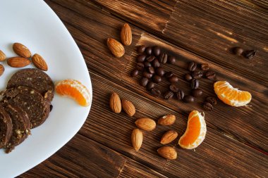 Badem fındık, kahve taneleri, mandalina dilimleri ve çikolata sosis pasta bir ahşap yüzeyde. Rustik natürmort.                               