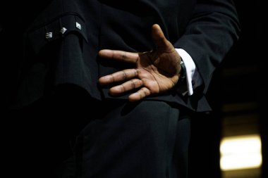 Şık bir takım elbise siyah bir adam elini onun arkasından değil merhaba demek isteyen sakladı. İletişim, yalıtım ve hipotermi korkusu. Karanlık bir arka plan üzerinde.                               