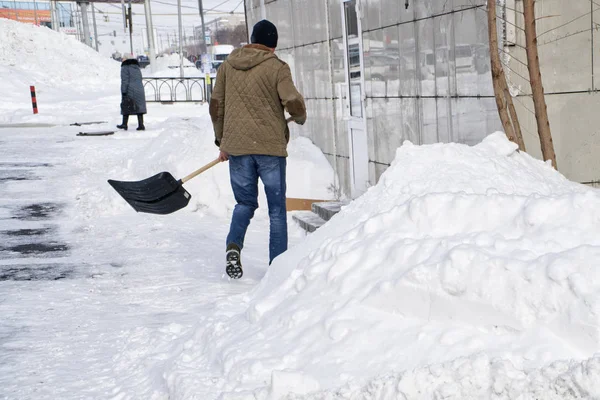 Молодий чоловік з лопатою очищає міську вулицю після весняного снігопаду — стокове фото