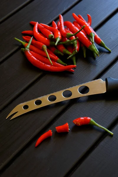 Los chiles rojos en rodajas y un cuchillo de verduras y queso yacen sobre una superficie de madera negra . — Foto de Stock