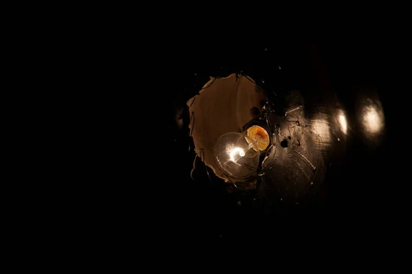 A dim incandescent lamp shines through a black hole in the ceiling.