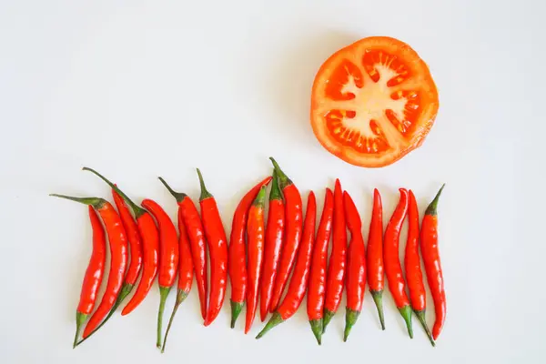 Baljor av röda chilipeppar och hälften en tomat ligga på en vit yta. Krydda och hälsosam mat. Fritt utrymme för inskriptioner. — Stockfoto