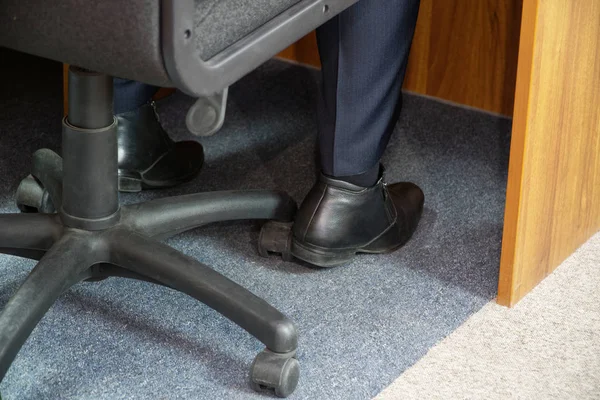 The legs of a man sitting in an office chair while on duty at work.