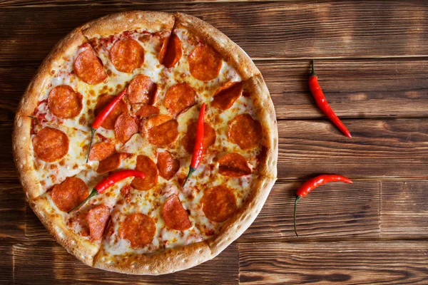 In Scheiben geschnittene hausgemachte Pizza mit Peperoni und roten Chilischoten liegt auf einer natürlichen Holzoberfläche aus Pinienbohlen. — Stockfoto