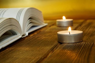 Din ve inanç hakkında açık bir kitap ahşap plakalar altın arka plan üzerinde yatıyor. Yakınlarda yanan mumlar bulunmaktadır.