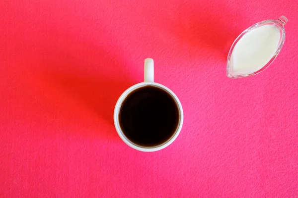 Tasse blanche avec café noir et une cruche de crème sur une surface rose — Photo
