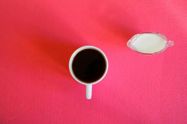 Une cruche de crème et une tasse blanche avec du café noir sur une surface rose. Vue d'en haut. Minimalisme. Géométrie . — Photo