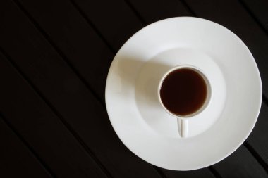 Siyah çay beyaz bir fincan koyu ahşap bir sekme üzerinde bir tabak duruyor