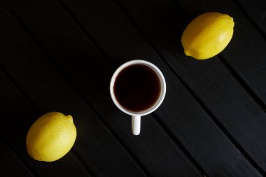 Siyah çay ve koyu bir tahtanın üzerinde iki sarı limon. 