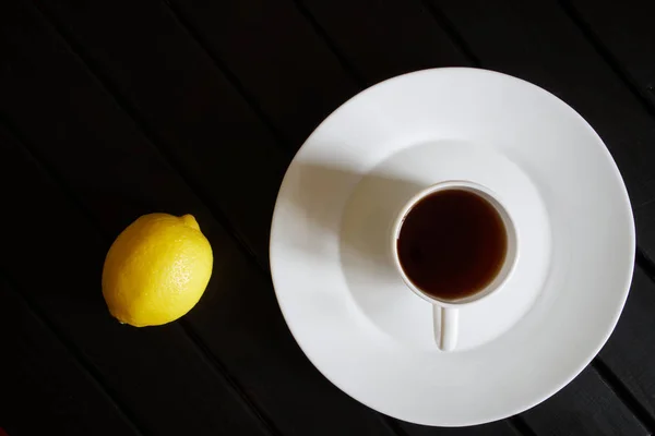 Une tasse blanche avec du thé noir se tient dans une soucoupe à côté d'un l jaune — Photo