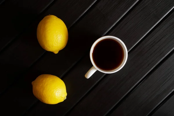 Uma xícara branca com chá preto fica em uma mesa preta ao lado de dois anos — Fotografia de Stock