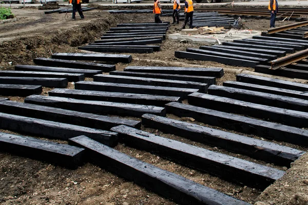 Workers are installing in a trench black wooden sleepers for tra
