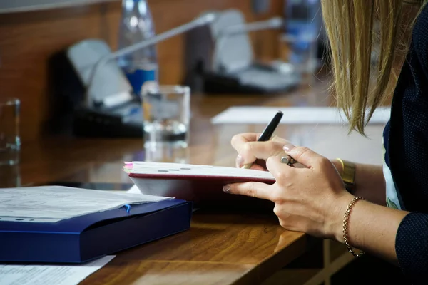 Una giovane donna con un braccialetto d'oro scrive appunti in un noteb spesso — Foto Stock