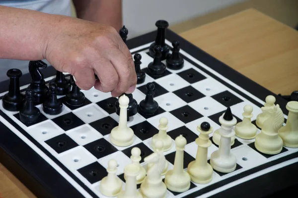 An elderly man plays chess. Special set of figures for the blind