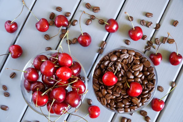 Grains de café torréfiés à côté de cerises rouges sur un fond clair — Photo