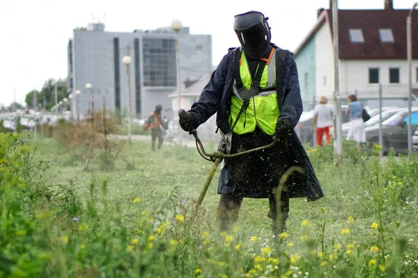 A man in a protective suit mows the grass with a handheld portab — Stock Photo, Image