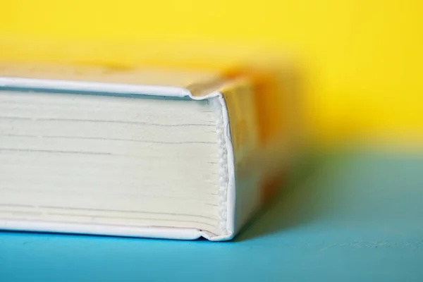 A closed thick white book or diary lies on a yellow and blue bac — Stock Photo, Image