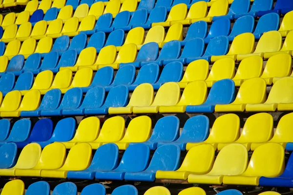 Багато використовуваних синіх і жовтих пластикових сидінь на відкритому стадіоні. Ф'юрі — стокове фото