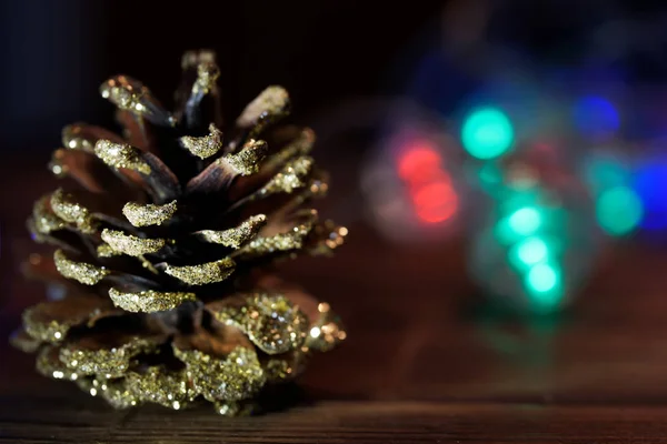 Un cono decorato con paillettes di una conifera giace su un su di legno — Foto Stock