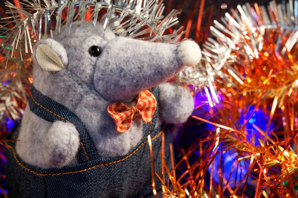 A plush mouse next to Christmas tinsel and LED lights. A symbol