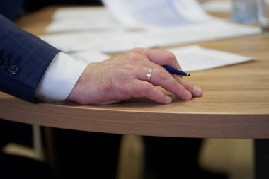 The hand of a male leader holds a fountain pen during an important meeting or filling out documents. Decision making. Sight and signing. Close-up clipart