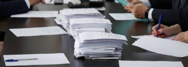 A lot of papers or ballots are on the table, where officials or businessmen are sitting. Counting of votes. Reportage. Panorama. No face clipart