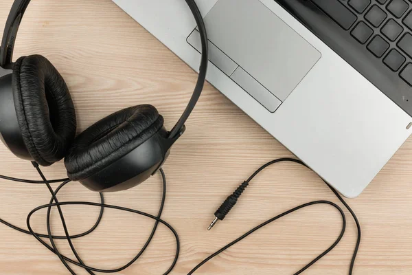 Black headphone and laptop computer on wooden background. Headphones with laptop. View from above