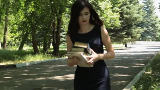 Дівчина з книгами сідає на лавку, щоб читати книги — стокове відео