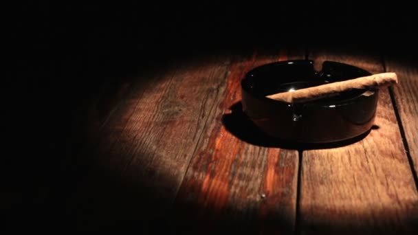 Horizontal panorama of a cigar lying in a black ashtray in the beam of light. — Stock Video