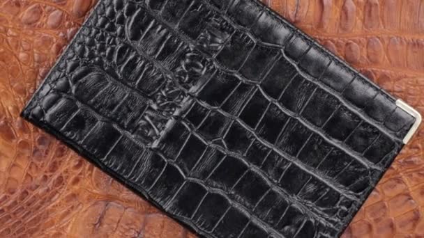 Rotatie, close-up zwarte dekking voor paspoort, liggend op bruin krokodilhuid. — Stockvideo