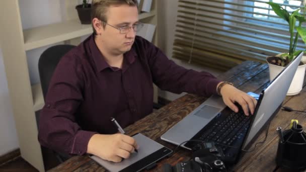 Grafisch ontwerper, grafisch tablet puttend uit terwijl het gebruiken van laptop in office. — Stockvideo